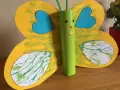 Papillon jaune aux ailes décorées de peinture à la paille, avec un corps vert en rouleau de papier toilette.