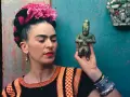 Frida Kahlo, avec ses fleurs roses et sa robe colorée, tient une statuette ancienne.