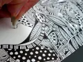 Main d'artiste créant un gribouillage artistique complexe, rempli de motifs géométriques et organiques en noir et blanc.