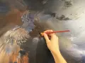 Main d'artiste travaillant sur une peinture à l'huile technique, ajoutant des détails à une figure aux ailes majestueuses.