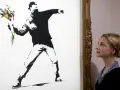 Une jeune femme admire "Flower Thrower", une œuvre emblématique de qui est Banksy, représentant un homme lançant un bouquet de fleurs.
