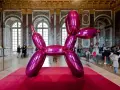 Une sculpture de chien ballon rose vif, une des œuvres d'art de Jeff Koons, trône sur un tapis rouge dans un grand hall orné.