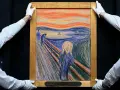 Deux hommes en gants blancs présentent le célèbre tableau "Le Cri" de Munch, avec son ciel orangé et sa figure angoissée.