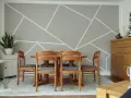 Un salon moderne avec un motif décoration peinture géométrique sur le mur. Une table en bois et des chaises grises sont disposées au centre.