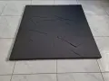 Une toile texturée, d'un noir absolu, aux courbes abstraites et profondes, posée sur un sol carrelé.