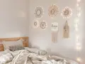 Un lit douillet avec des draps froissés, sur le mur, des miroirs soleil décoratifs et une guirlande lumineuse. Un tableau de nu noir et blanc est absent.