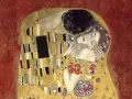 Le baiser de Klimt : un couple enlacé dans une étreinte dorée, sur fond rouge. L'homme enlace la femme, qui ferme les yeux, le visage baigné de lumière.