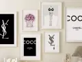 Un mur décoré de plusieurs tableaux, dont un tableau metal vintage avec le logo YSL noir sur fond noir, et des affiches Chanel.