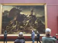 Un tableau crépuscule, "Le Radeau de la Méduse", montre des survivants désespérés sur un radeau. Des visiteurs contemplent cette œuvre dramatique.