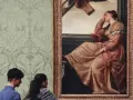 Deux visiteurs contemplent un tableau célèbre, une femme en robe rose, dans une galerie d'art aux murs tapissés.