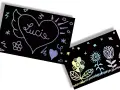 Un cœur ailé avec le nom "Lucie" et des fleurs colorées sur fond noir. Un **modèle dessin à gratter facile** pour s'amuser.