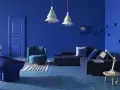 Un salon moderne aux murs et au sol bleu profond. Un canapé d'angle, un fauteuil, un pouf et une table basse complètent ce tableau déco bleu.