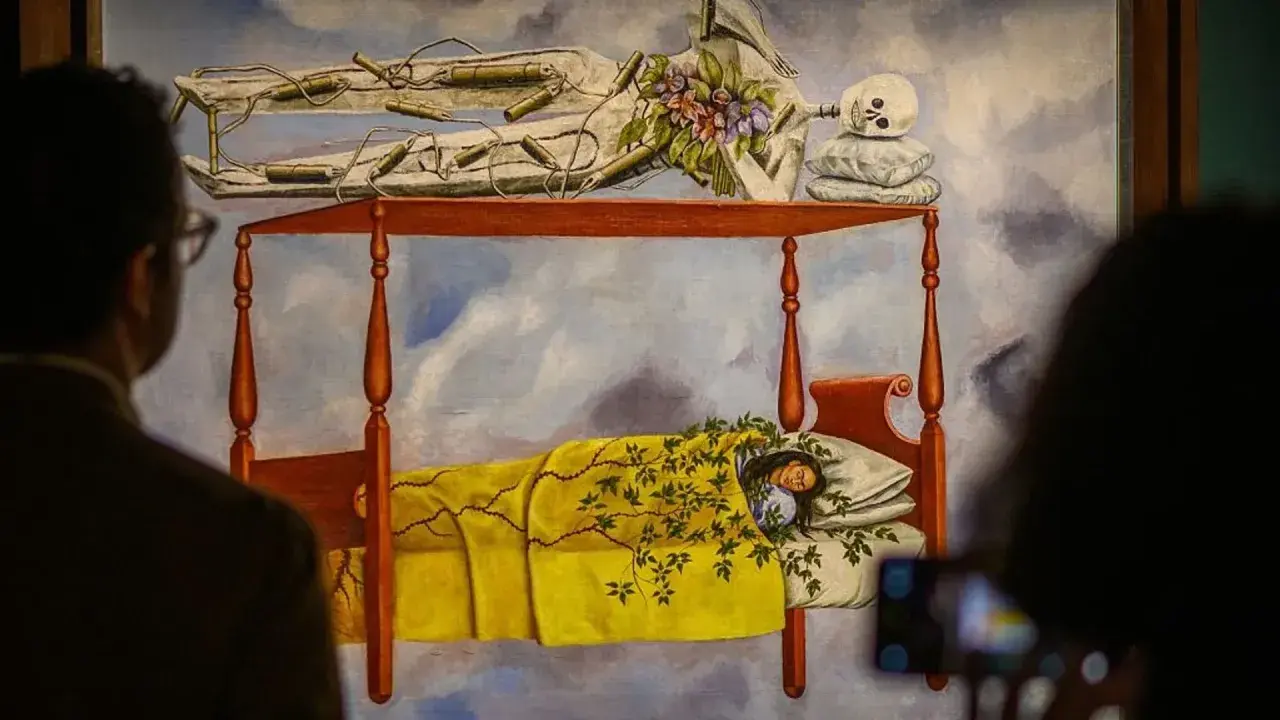 La peinture de Frida Kahlo "Le lit volant" montre une femme endormie sous une couverture jaune, avec un squelette au-dessus.