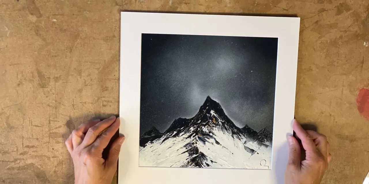 Des mains tiennent une œuvre d'art représentant des montagnes enneigées sous un ciel étoilé, rappelant le style des peintres contemporains.