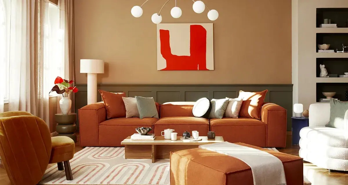 Salon cosy avec canapé orange, fauteuil velours et un tableau couleur chaude.