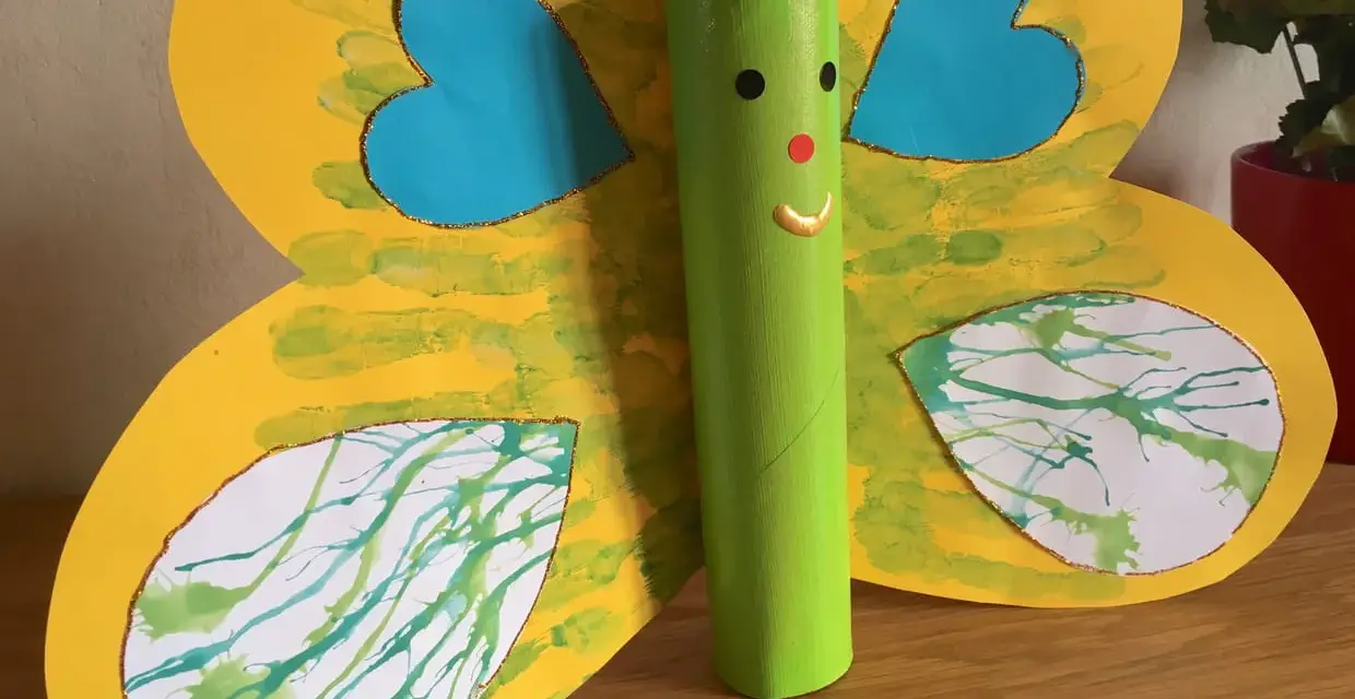 Papillon jaune aux ailes décorées de peinture à la paille, avec un corps vert en rouleau de papier toilette.