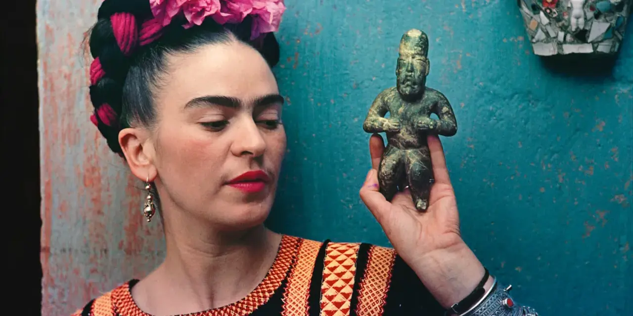 Frida Kahlo, avec ses fleurs roses et sa robe colorée, tient une statuette ancienne.