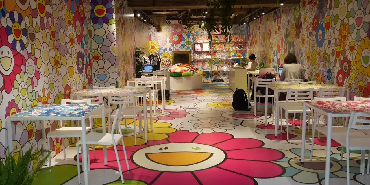 Un café aux couleurs vives, décoré de fleurs souriantes de l'artiste Murakami. Des tables et des chaises blanches invitent à s'asseoir dans cet univers joyeux.