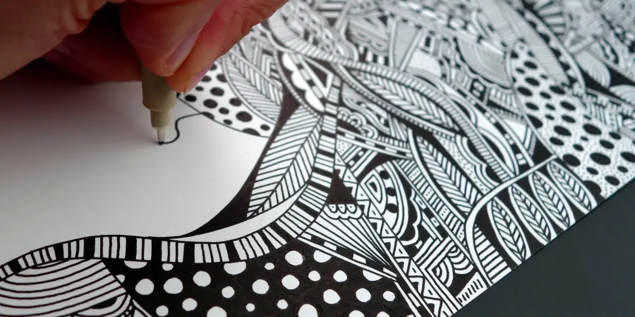 Main d'artiste créant un gribouillage artistique complexe, rempli de motifs géométriques et organiques en noir et blanc.