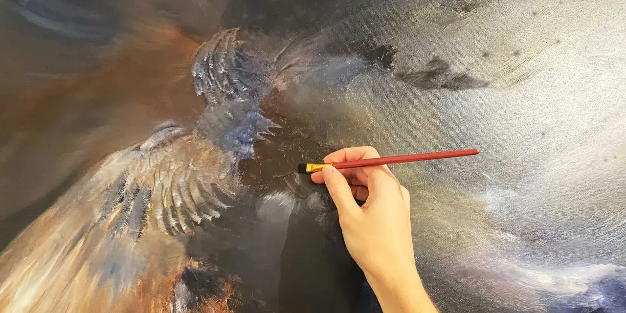 Main d'artiste travaillant sur une peinture à l'huile technique, ajoutant des détails à une figure aux ailes majestueuses.