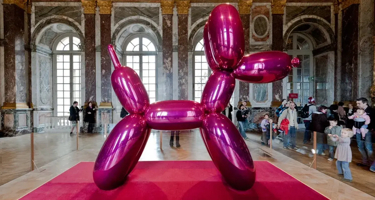 Une sculpture de chien ballon rose vif, une des œuvres d'art de Jeff Koons, trône sur un tapis rouge dans un grand hall orné.