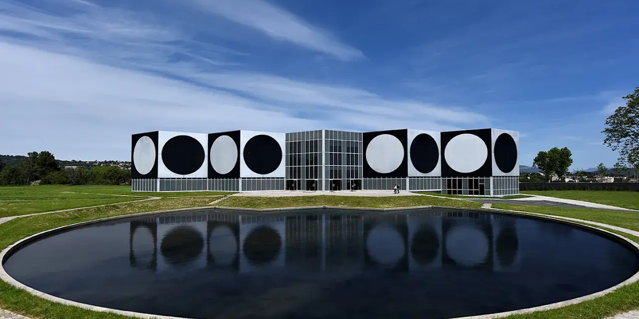 Le Centre d'art contemporain de Vassivière, avec ses façades ornées de cercles noirs et blancs, reflète les œuvres d'art de Victor Vasarely dans un étang paisible.