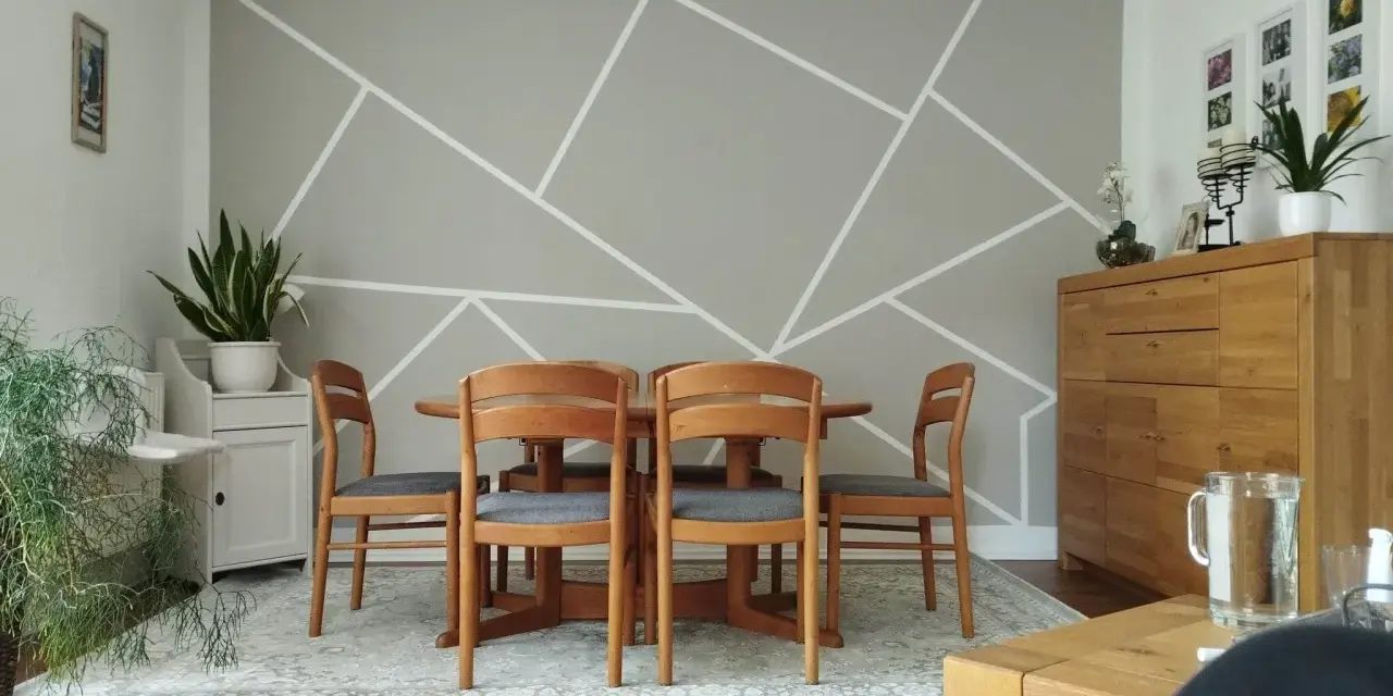 Un salon moderne avec un motif décoration peinture géométrique sur le mur. Une table en bois et des chaises grises sont disposées au centre.