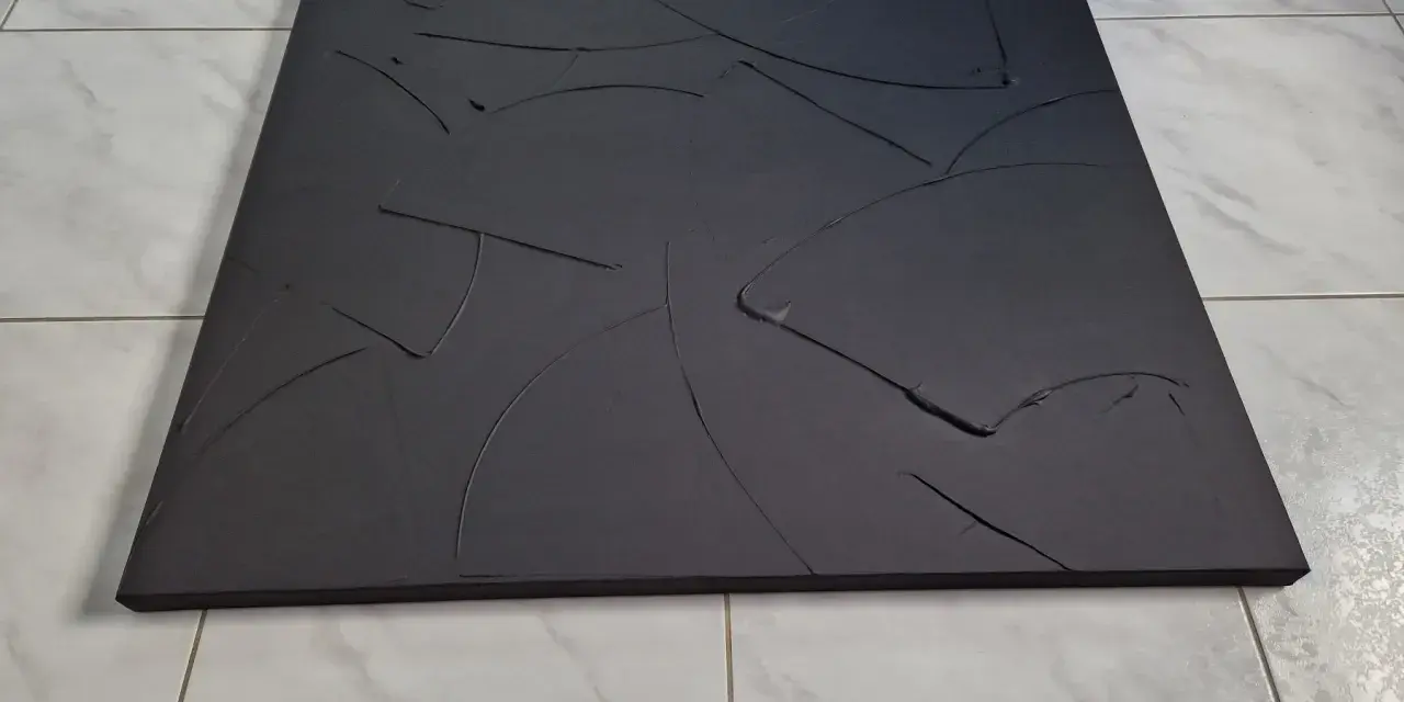 Une toile texturée, d'un noir absolu, aux courbes abstraites et profondes, posée sur un sol carrelé.