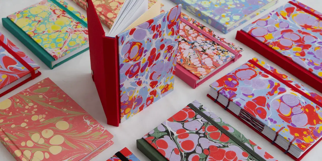 Collection de carnets aux motifs marbrés colorés, évoquant le motif Annonay. Des couleurs vives et des formes organiques se mélangent sur les couvertures.