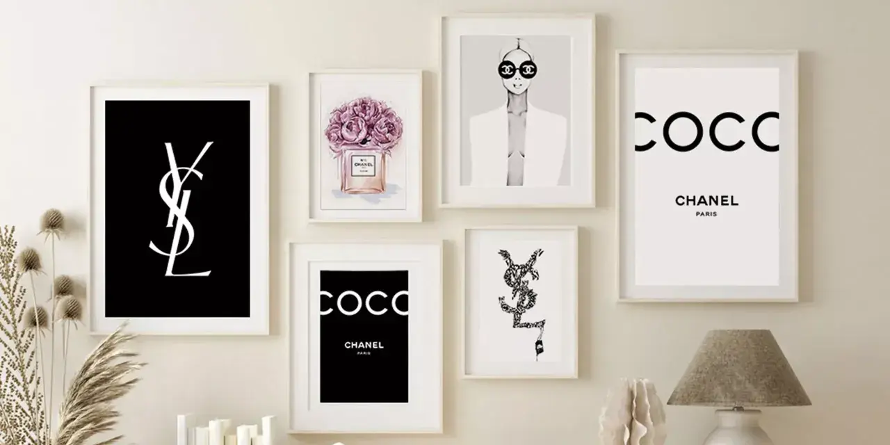 Un mur décoré de plusieurs tableaux, dont un tableau metal vintage avec le logo YSL noir sur fond noir, et des affiches Chanel.