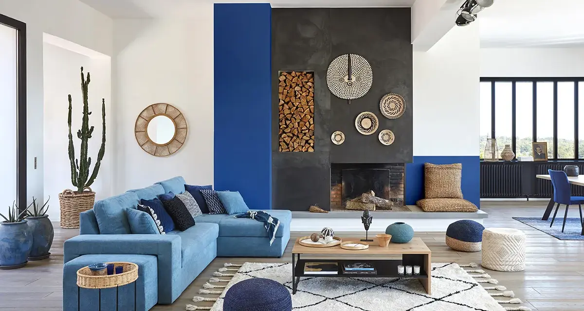 Un salon moderne avec un grand canapé bleu, une cheminée imposante et un tableau bleu marine sur le mur.