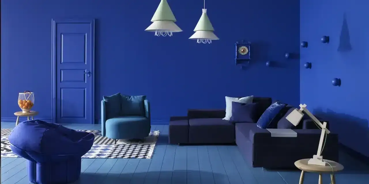 Un salon moderne aux murs et au sol bleu profond. Un canapé d'angle, un fauteuil, un pouf et une table basse complètent ce tableau déco bleu.