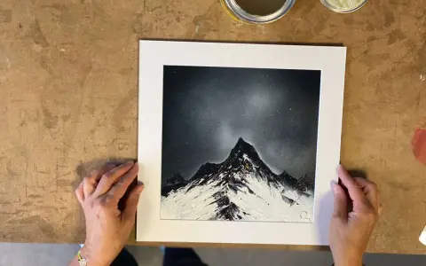 Des mains tiennent une œuvre d'art représentant des montagnes enneigées sous un ciel étoilé, rappelant le style des peintres contemporains.