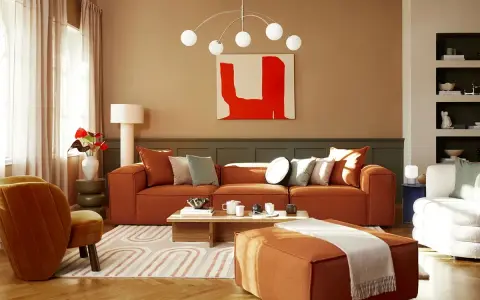 Salon cosy avec canapé orange, fauteuil velours et un tableau couleur chaude.