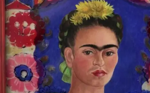 Portrait de Frida Kahlo, icône féministe, ornée de fleurs jaunes et d'un ruban vert, sur fond bleu vibrant et motifs floraux colorés.