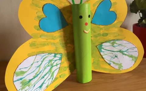 Papillon jaune aux ailes décorées de peinture à la paille, avec un corps vert en rouleau de papier toilette.