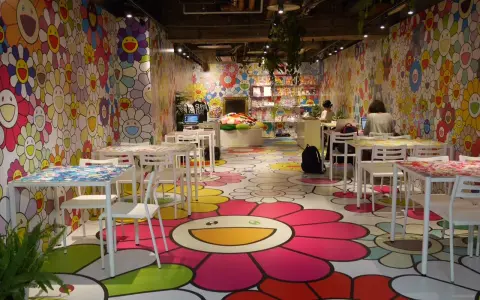 Un café aux couleurs vives, décoré de fleurs souriantes de l'artiste Murakami. Des tables et des chaises blanches invitent à s'asseoir dans cet univers joyeux.