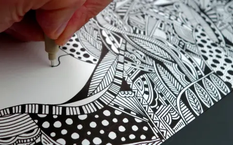 Main d'artiste créant un gribouillage artistique complexe, rempli de motifs géométriques et organiques en noir et blanc.