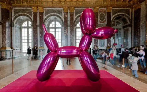 Une sculpture de chien ballon rose vif, une des œuvres d'art de Jeff Koons, trône sur un tapis rouge dans un grand hall orné.