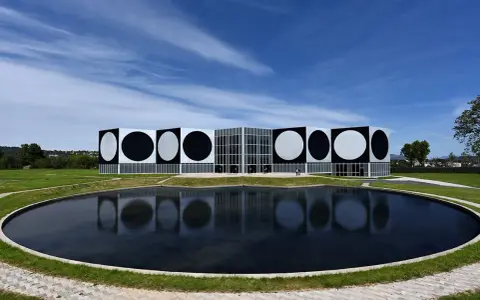 Le Centre d'art contemporain de Vassivière, avec ses façades ornées de cercles noirs et blancs, reflète les œuvres d'art de Victor Vasarely dans un étang paisible.