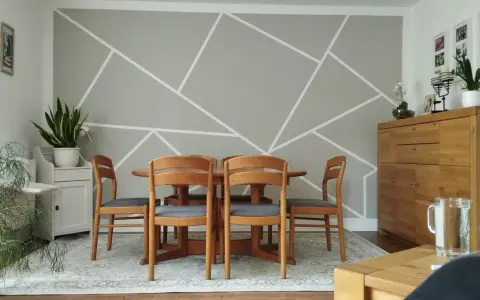 Un salon moderne avec un motif décoration peinture géométrique sur le mur. Une table en bois et des chaises grises sont disposées au centre.