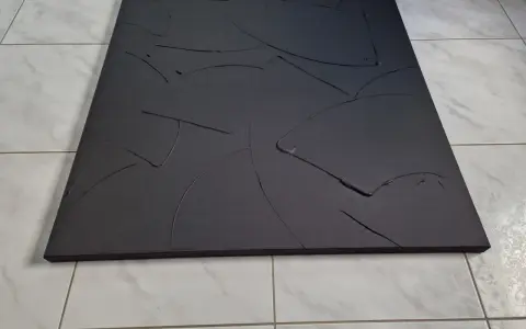 Une toile texturée, d'un noir absolu, aux courbes abstraites et profondes, posée sur un sol carrelé.