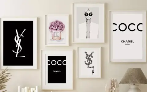 Un mur décoré de plusieurs tableaux, dont un tableau metal vintage avec le logo YSL noir sur fond noir, et des affiches Chanel.