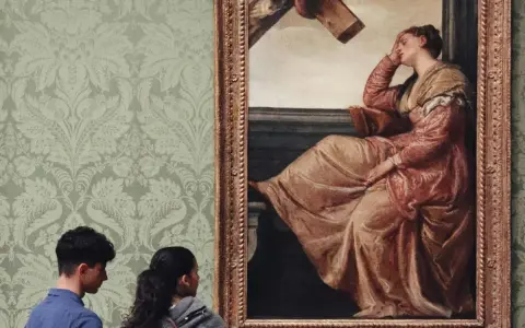 Deux visiteurs contemplent un tableau célèbre, une femme en robe rose, dans une galerie d'art aux murs tapissés.