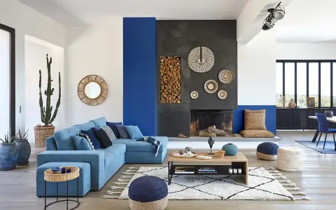 Un salon moderne avec un grand canapé bleu, une cheminée imposante et un tableau bleu marine sur le mur.
