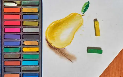 Une boîte de pastels secs pour débutant, avec une poire jaune esquissée sur du papier blanc, et des pastels jaune et vert à côté.
