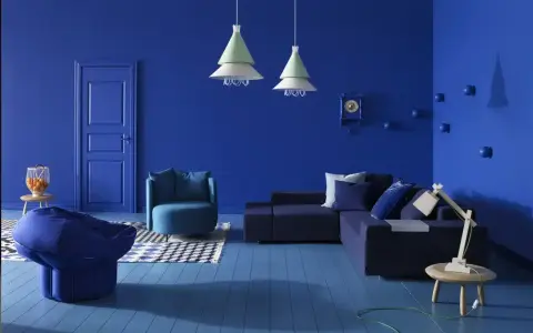 Un salon moderne aux murs et au sol bleu profond. Un canapé d'angle, un fauteuil, un pouf et une table basse complètent ce tableau déco bleu.