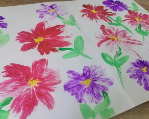 Des fleurs peintes en relief, rouges et violettes, avec des touches de jaune au centre. Une technique simple pour apprendre comment peindre des fleurs en relief.