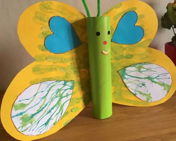 Papillon jaune aux ailes décorées de peinture à la paille, avec un corps vert en rouleau de papier toilette.