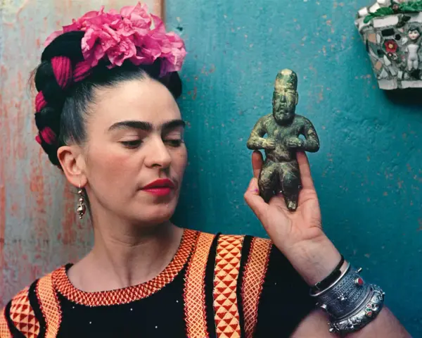 Frida Kahlo, avec ses fleurs roses et sa robe colorée, tient une statuette ancienne.